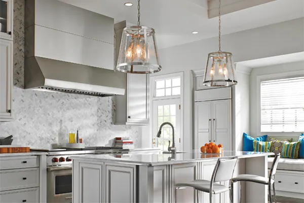 Pictured are two lustrous pendants in polished nickel with glass shades hanging over a kitchen island.