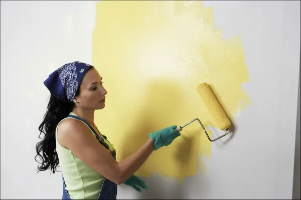 Woman Painting A White Wall Yellow To Update The Spring Cleaning